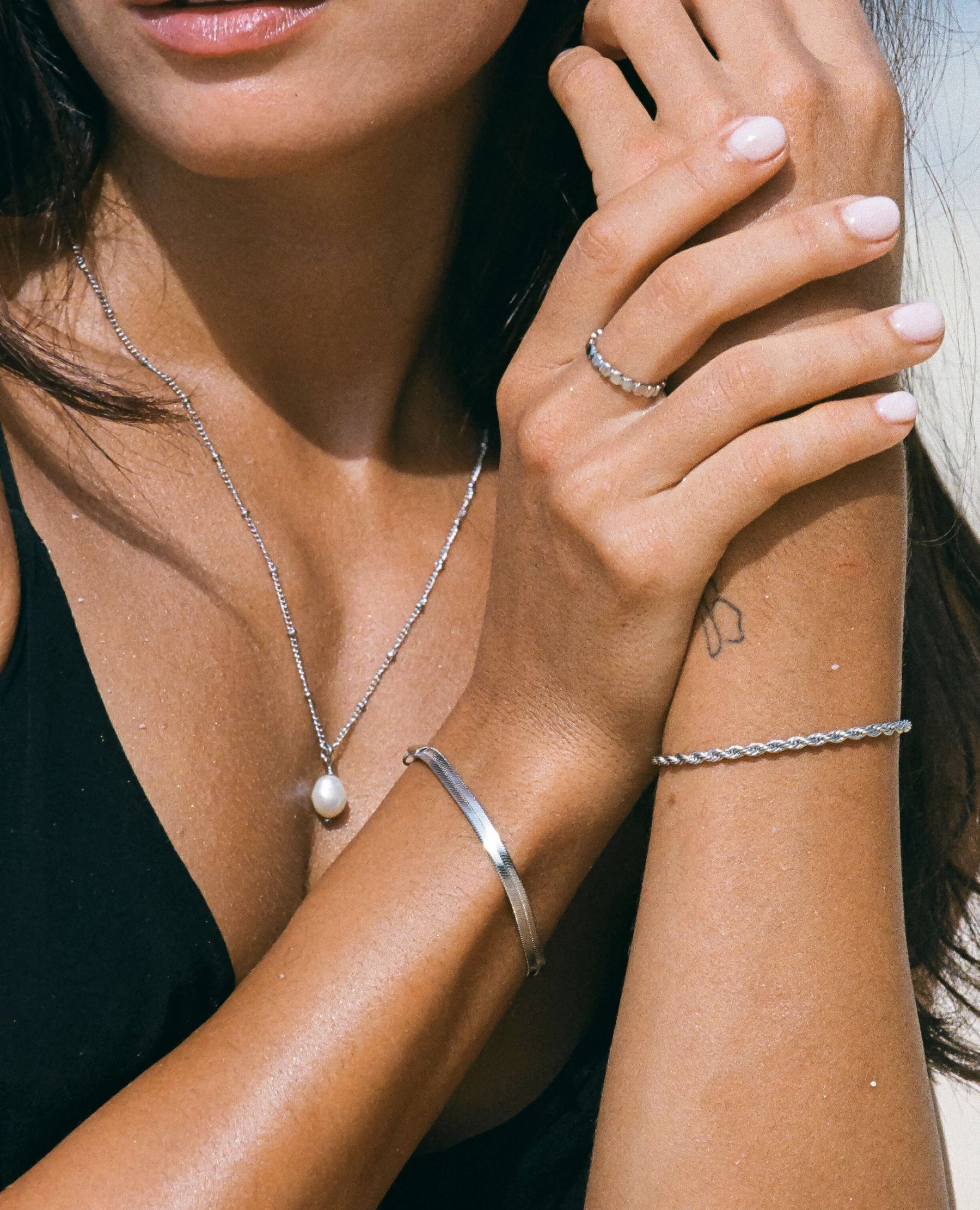 Close-up of a woman's hands wearing silver jewelry, including a ring, bracelet, and necklace.